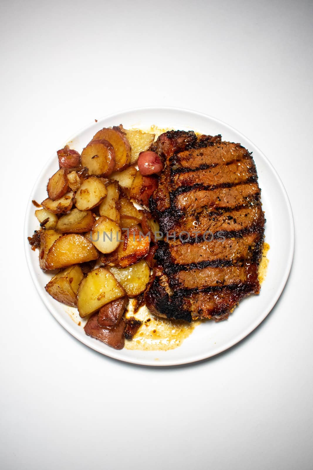 A Perfectly Grilled Steak With Black Grill Lines and Potatoes Plated on a Pure White Background