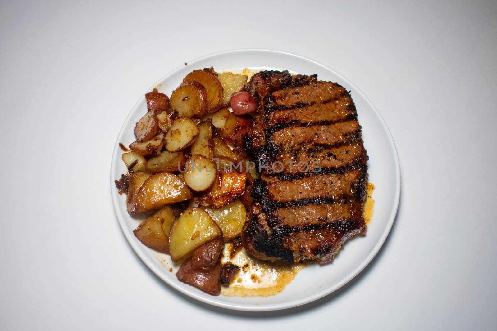 A Perfectly Grilled Steak With Black Grill Lines and Potatoes Plated on a Pure White Background