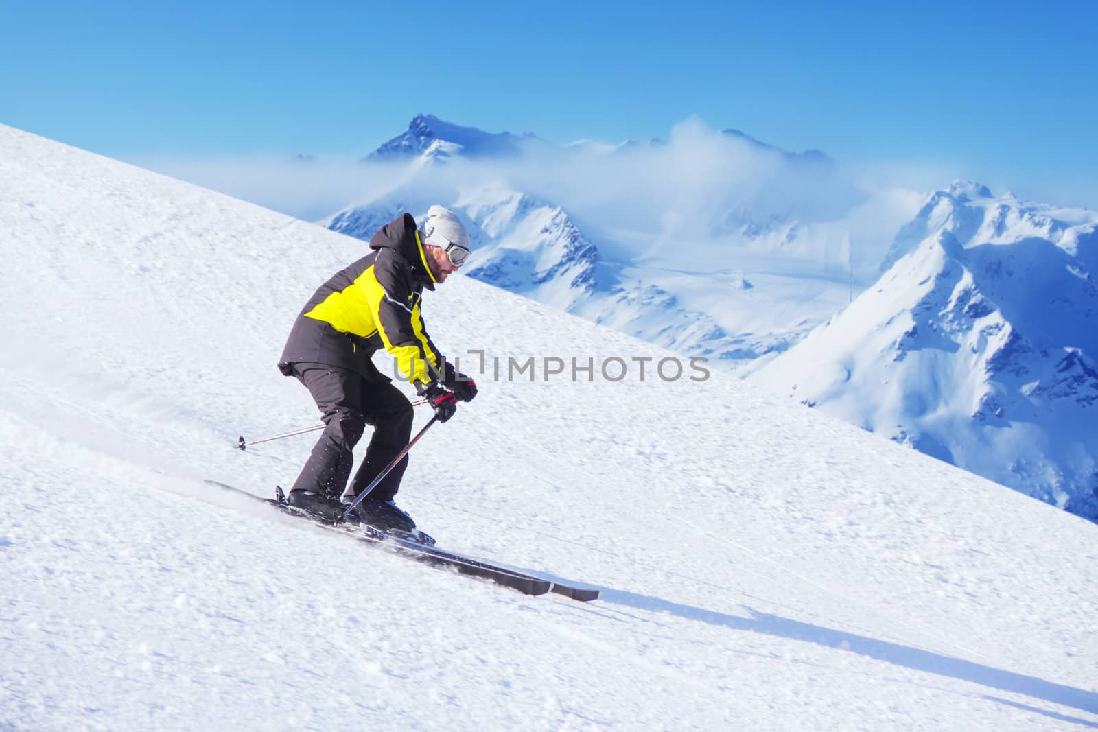 Alpine giant slalom skier on piste running downhill in beautiful Alpine landscape. Blue sky on background. Free copy space for text