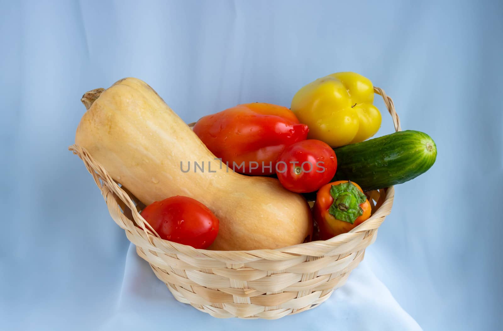 Wicker basket with different vegetables. Pumpkin, pepper, cucumber, tomatoes.Isolated on a blue background.The concept of crop.