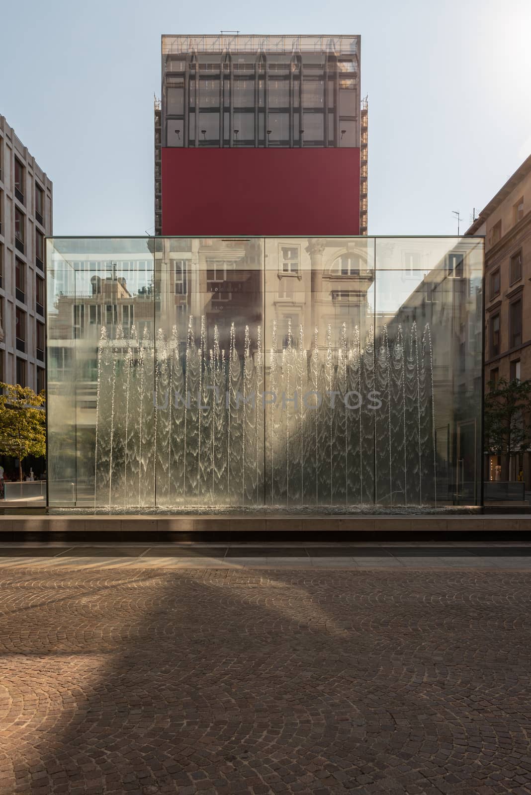 Modern fountain with water splashes on a huge glass window cut by the shadow, contemporary architecture in the city center