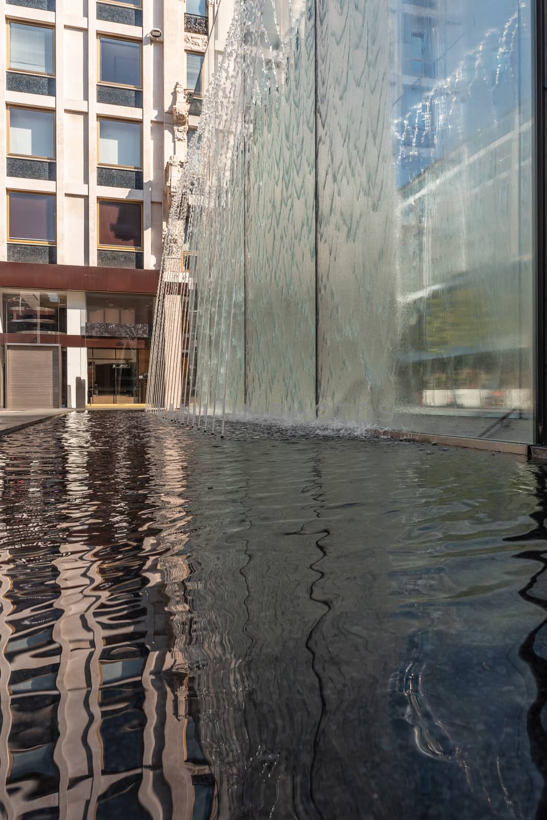 Modern fountain with water splashes on a huge glass window by brambillasimone