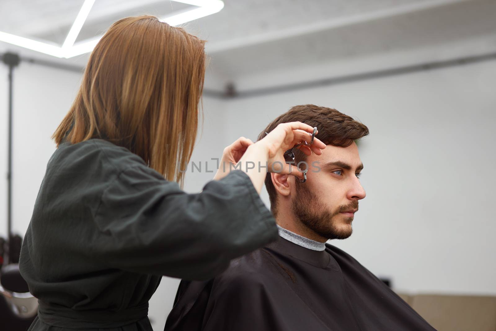 Stylish man sitting barber shop Hairstylist Hairdresser Woman cutting his hair Portrait handsome happy young bearded caucasian guy getting trendy haircut Attractive barber girl working serving client