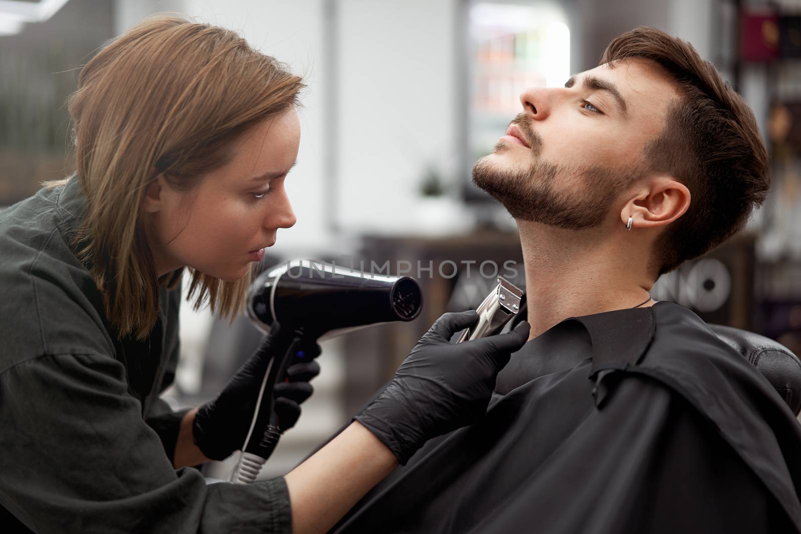 Stylish man sitting barber shop Hairstylist Hairdresser Woman blow dry his hair Portrait handsome happy young bearded caucasian guy getting trendy haircut Attractive barber girl serving client