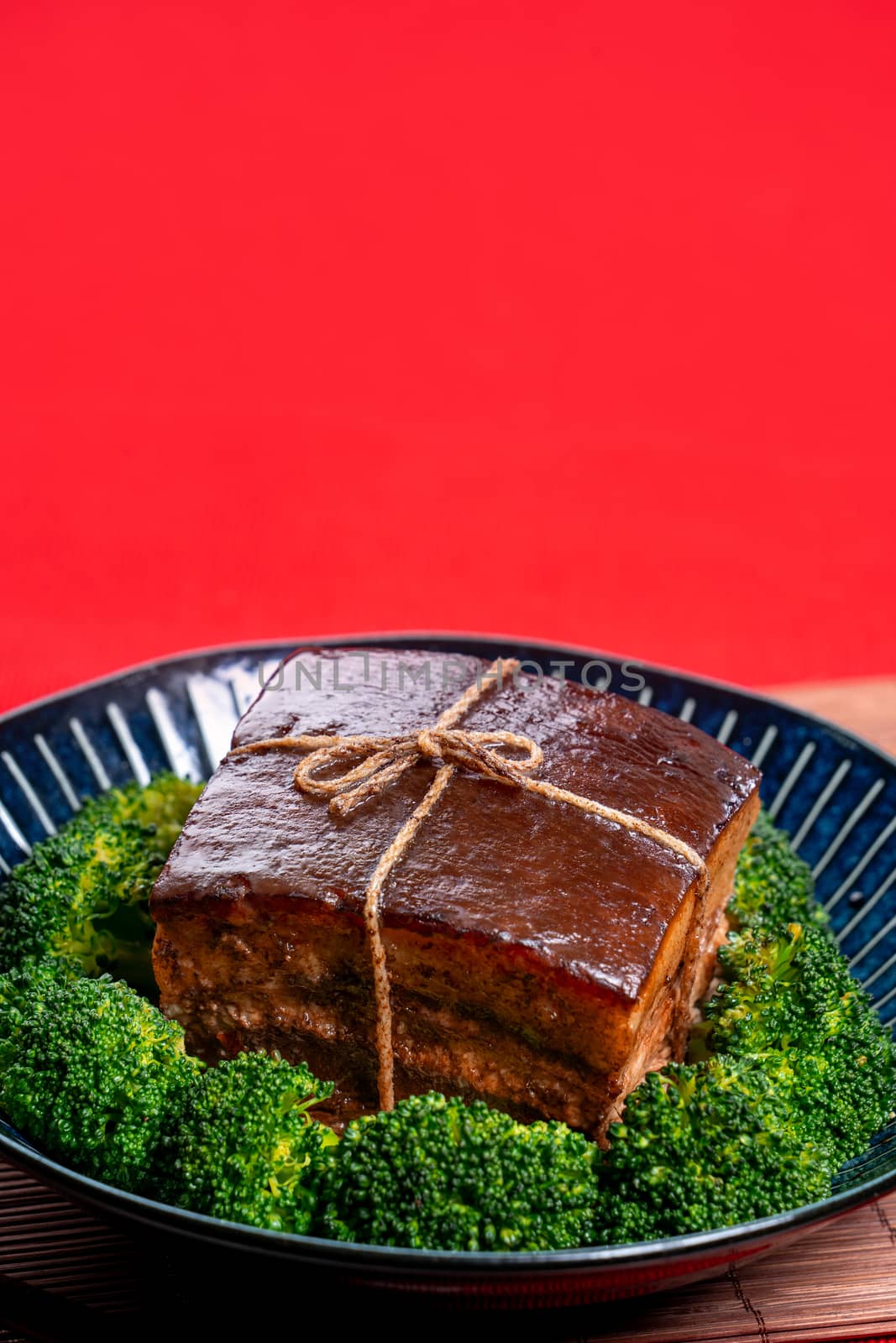 Dong Po Rou (Dongpo pork meat) in a beautiful blue plate with green broccoli vegetable, traditional festive food for Chinese new year cuisine meal, close up.