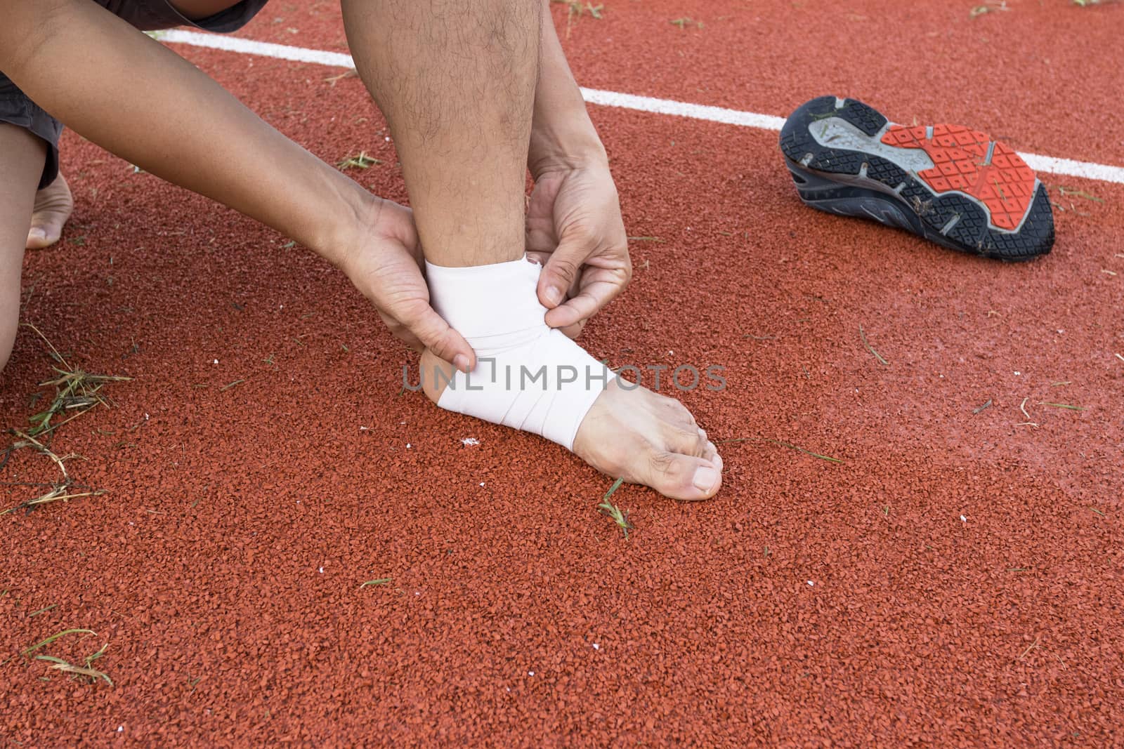 man applying compression bandage onto ankle injury of a football player, Sports injuries, concept First aid for ankle injuries