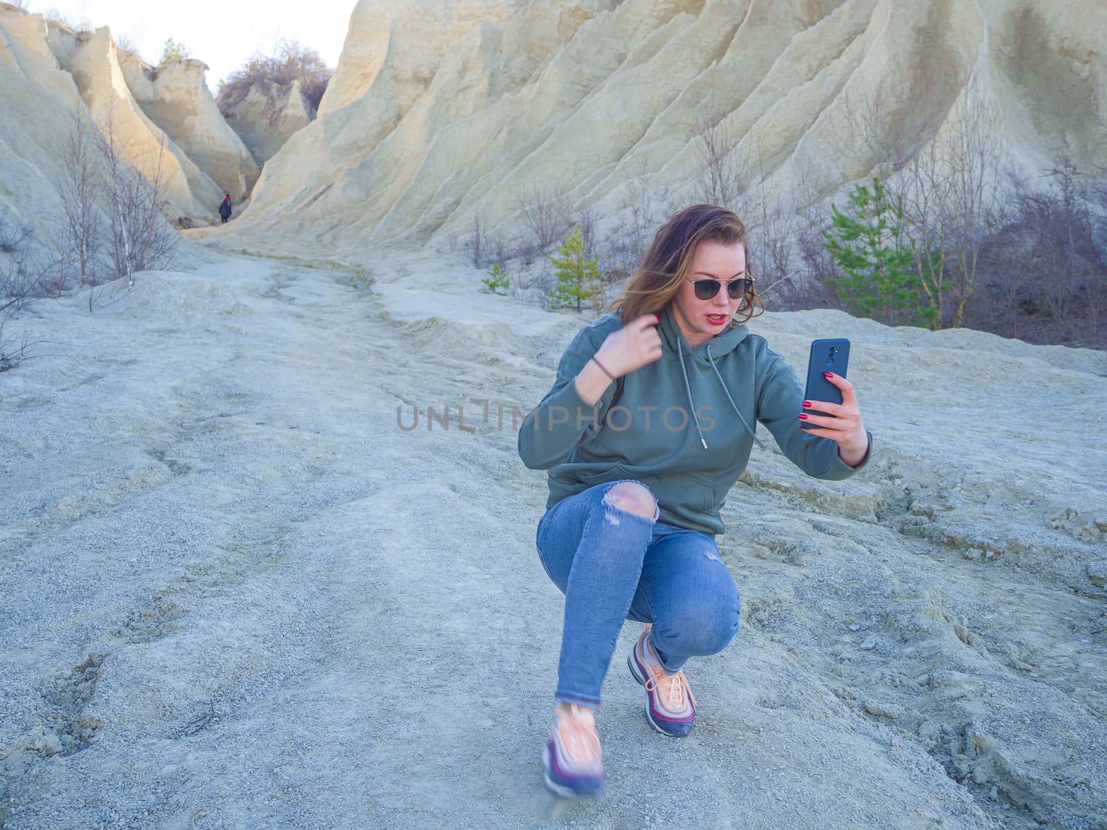 Hiker on mountain top with smartphone. Woman is standing and taking a picture on smartphone. Abandoned Quarry Of Rummu, Estonia. Scenic View Of Land Against Clear Blue Sky. Panoramic View.