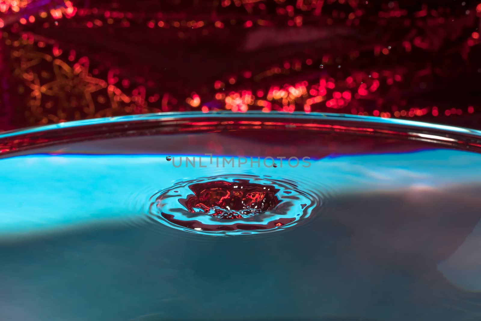 Splash of water on an abstract red backgrounds close up.A frozen drop of water is photographed at high speed.The slow dripping of the liquid with the air bubbles.Nature backgrounds.Frozen drip liquid