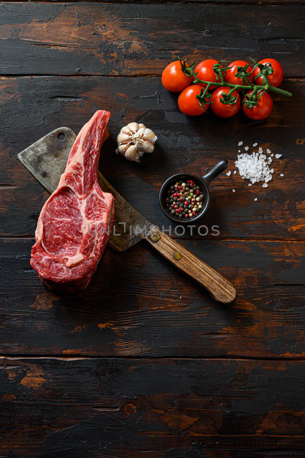 Raw Beef Rib Steak on meat cleaver. Organic farm marbled prime black angus beef. Dark wooden background. top view. With seasonings, peppercorns, rosemary,salt,garlic. space for text noone