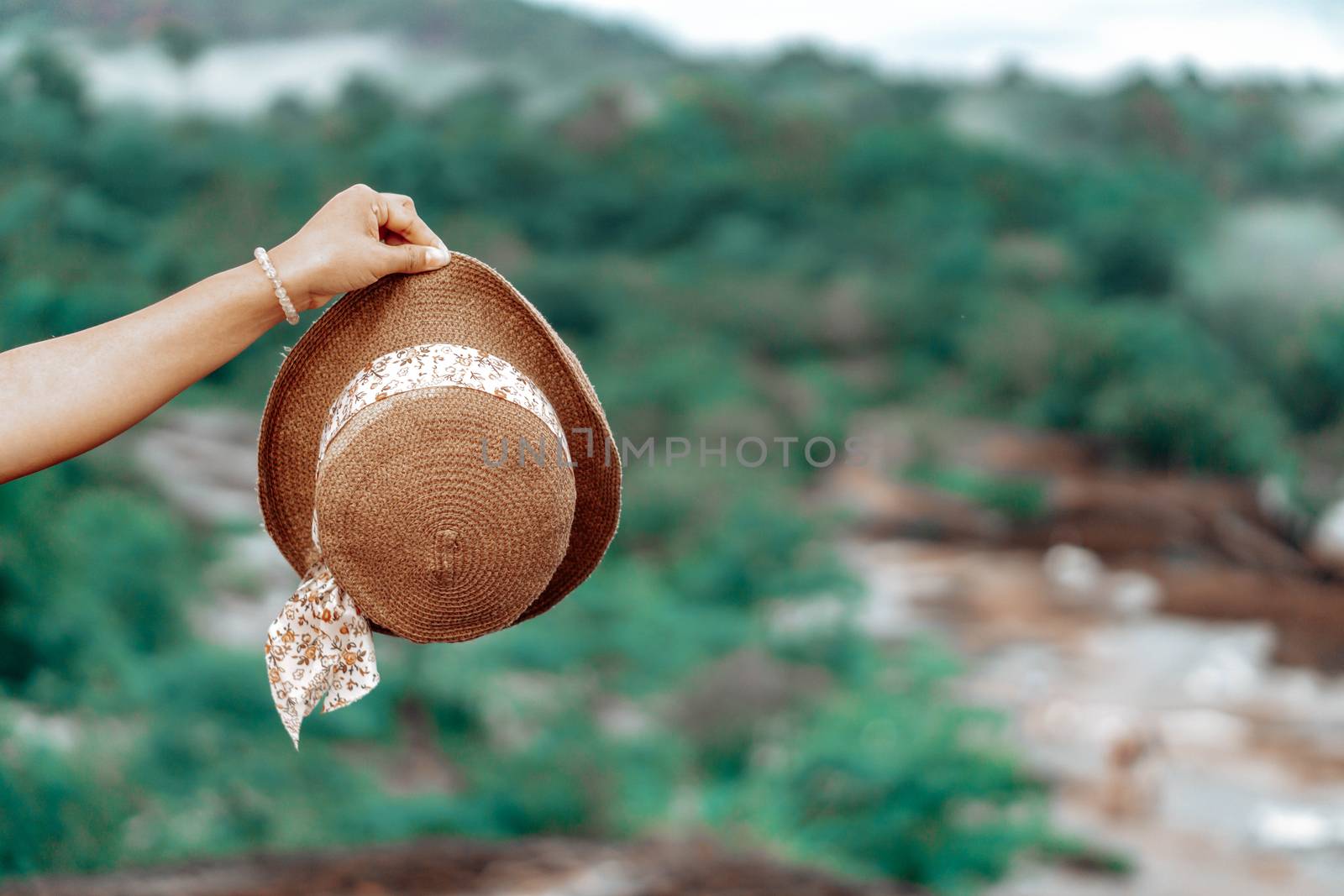 Woman hand holding hat with green nature background, travel concept