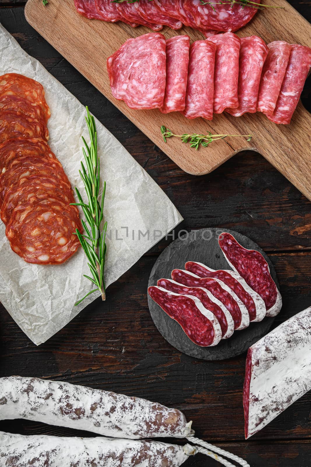 Variety of dry cured chorizo, fuet and other sausages cut in slices with herbs on old wooden table, top view.