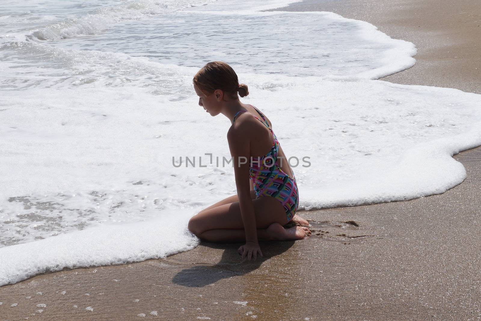 teenage girl sitting alone on the wet sand and looking at the sea.