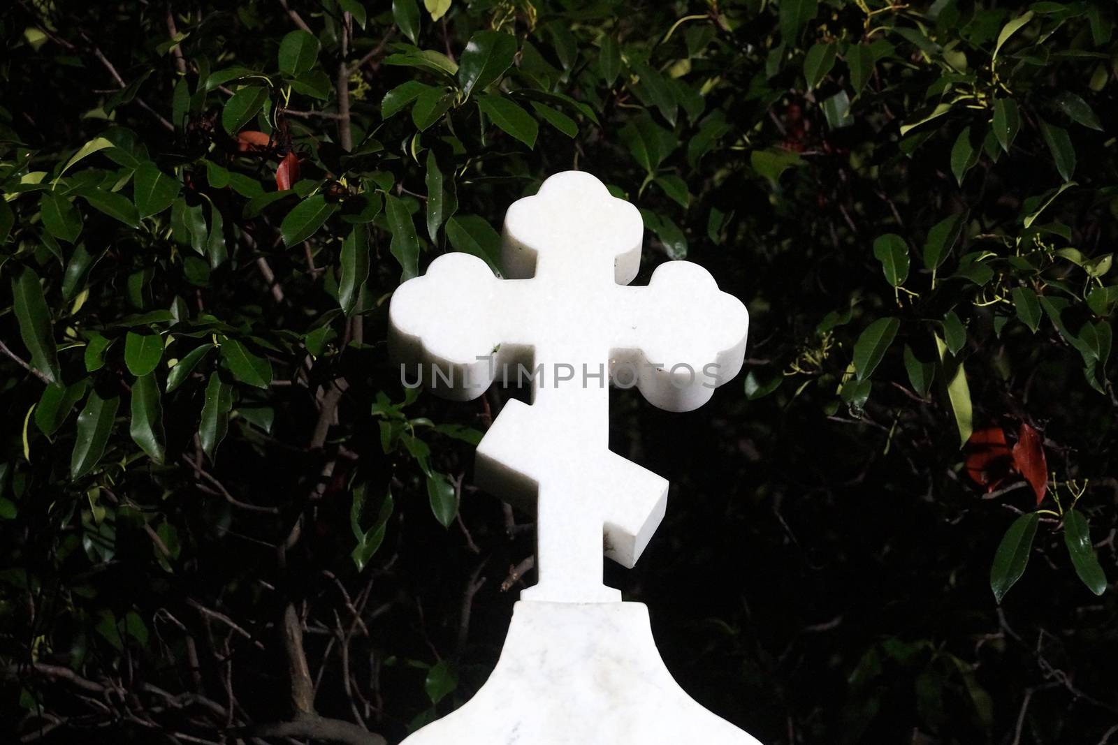 white orthodox marble cross on the grave against the background of a dark forest.