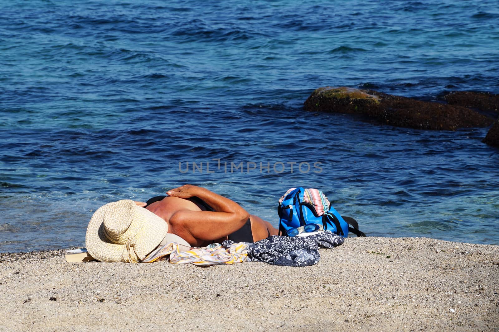 aged woman sunbathes on the sea beach by Annado