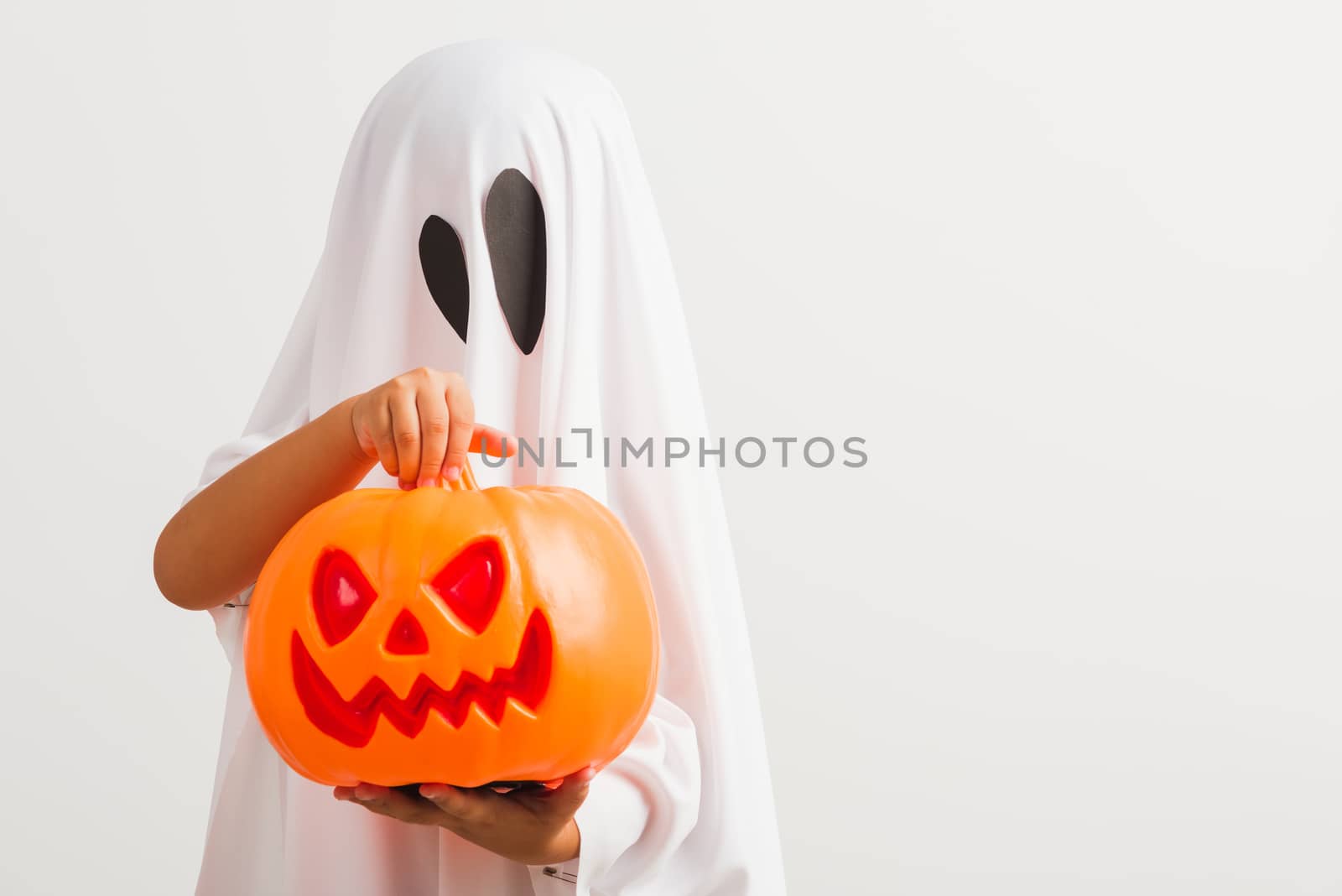 Funny Halloween Kid Concept, little cute child with white dressed costume halloween ghost scary he holding orange pumpkin ghost on hand, studio shot isolated on white background