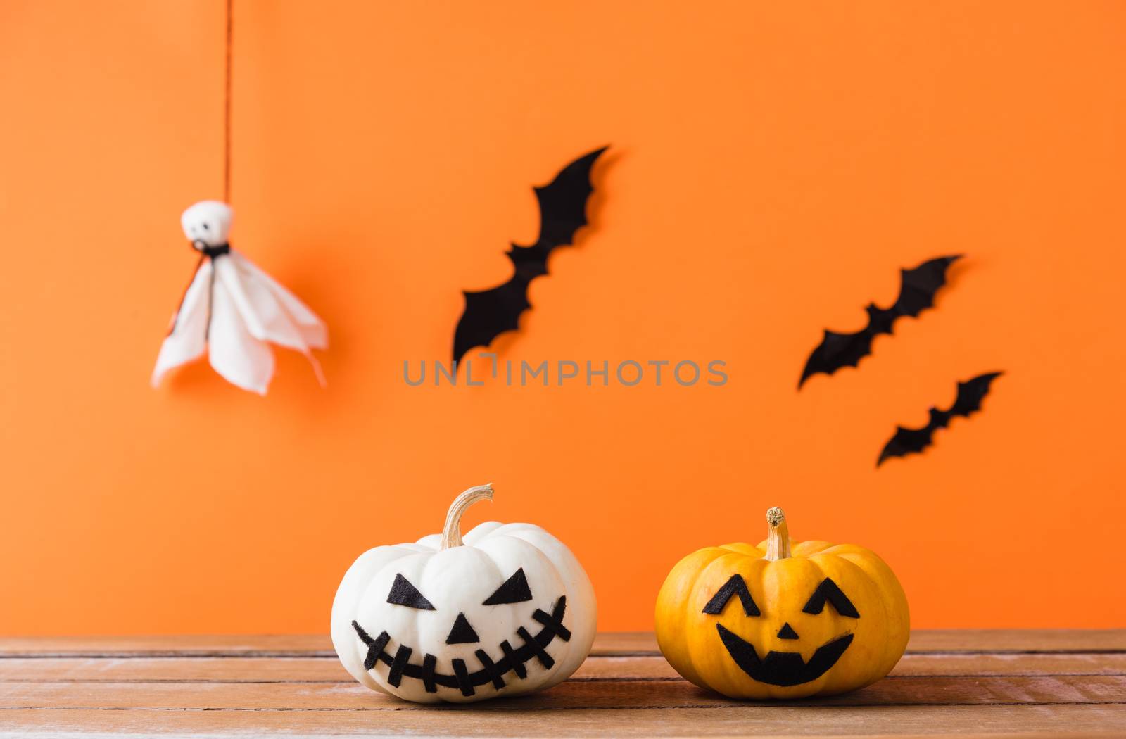 Funny Halloween day decoration party, Cute pumpkin ghost spooky jack o lantern face, black spider and bats on wooden table, studio shot isolated on an orange background, Happy holiday concept