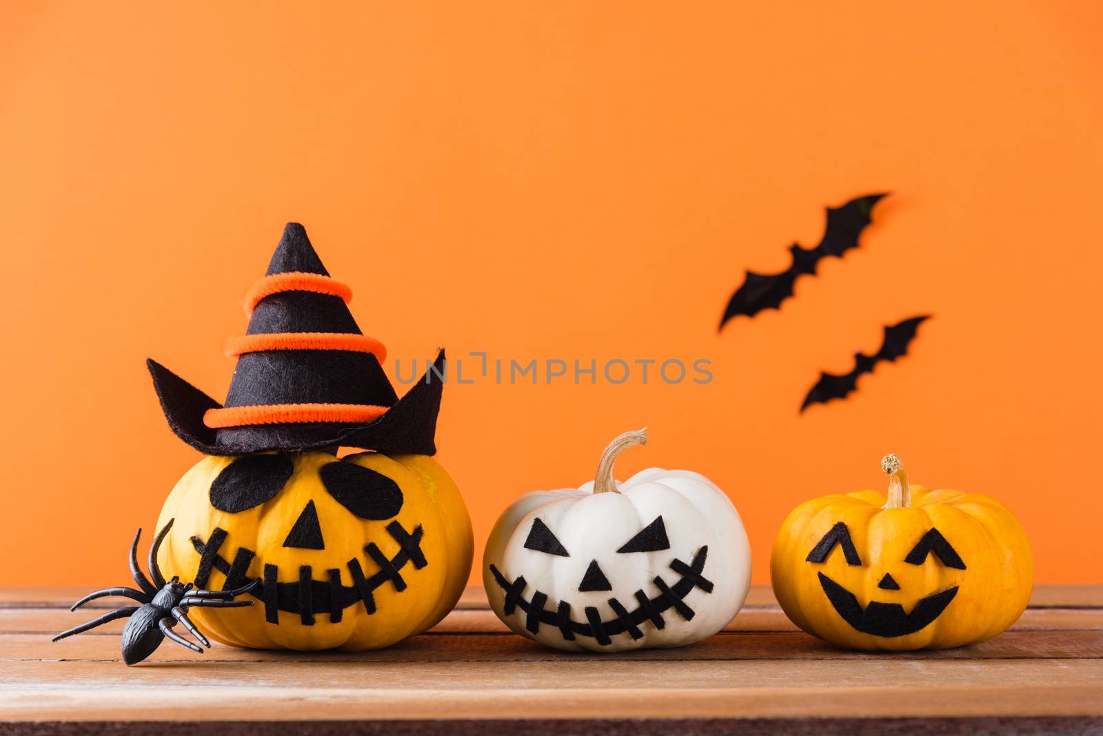 Funny Halloween day decoration party, Cute pumpkin ghost scary jack o lantern face, black spider and bats on wooden table, studio shot isolated on an orange background, Happy holiday concept