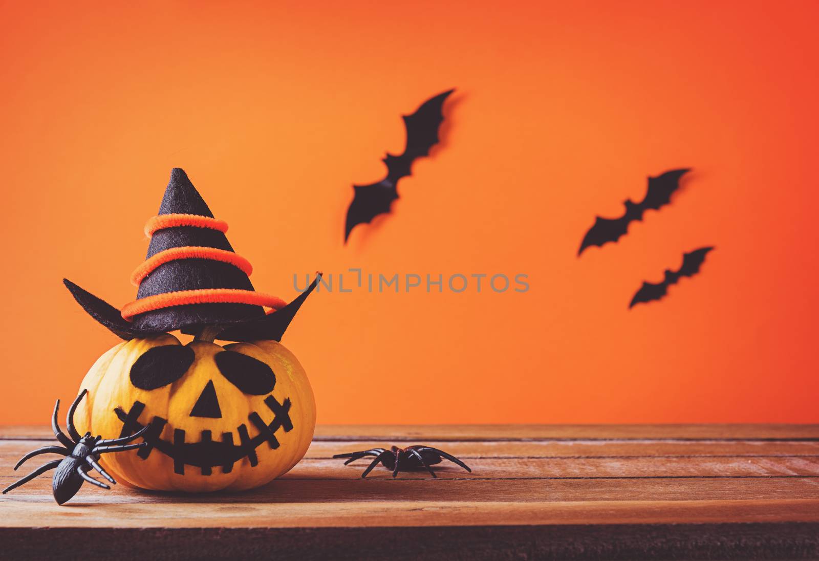 Funny Halloween day decoration party, Cute pumpkin ghost spooky jack o lantern face wear hat, black spider and bats on wooden table, studio shot isolated on an orange background, Happy holiday concept