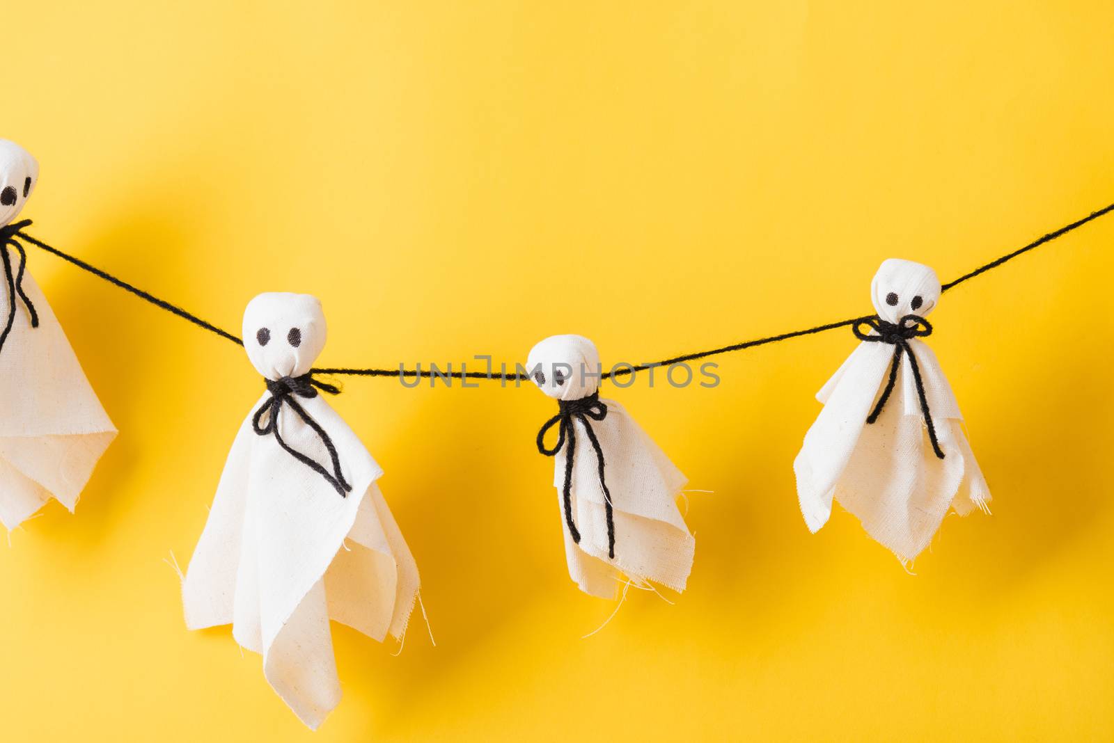 Funny Halloween day decoration party, Full body of baby cute white ghost crafts scary face hanging, studio shot isolated on yellow background, Happy holiday DIY handicraft concept