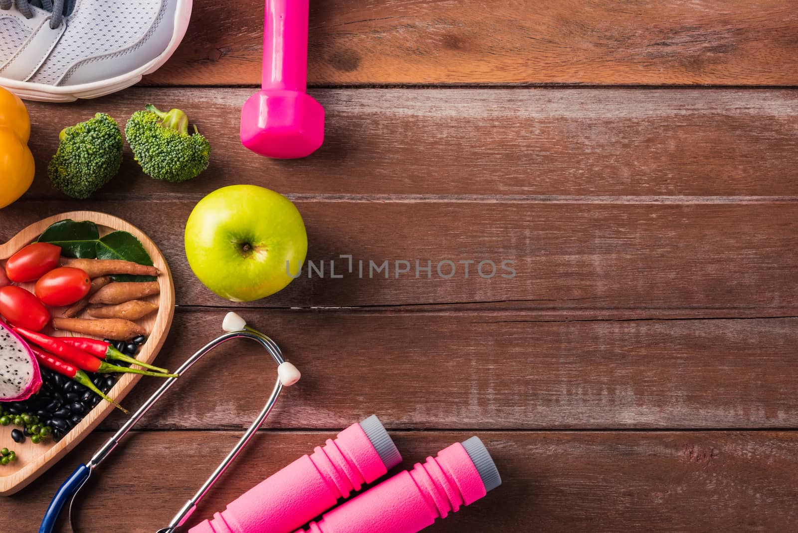 Top view of fresh organic fruit and vegetable in heart plate, shoes, sports equipment and doctor stethoscope, studio shot on wooden gym table, Healthy diet vegetarian food concept, World food day