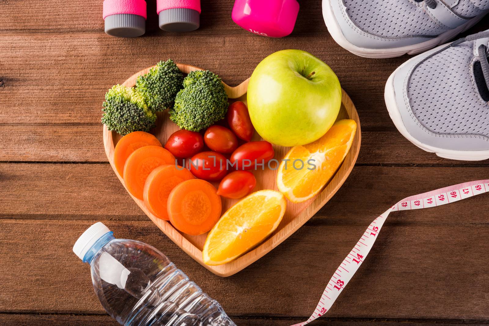 Top view of fresh fruits and vegetables in heart plate wood (apple, carrot, tomato, orange, broccoli) and dumbbells, sport shoes sports equipment on wooden table, Healthy lifestyle diet food concept