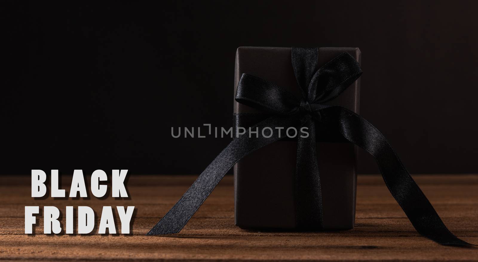 Black Friday sale concept, Gift box wrapped in black paper and black bow ribbon on wooden table studio shot on black background