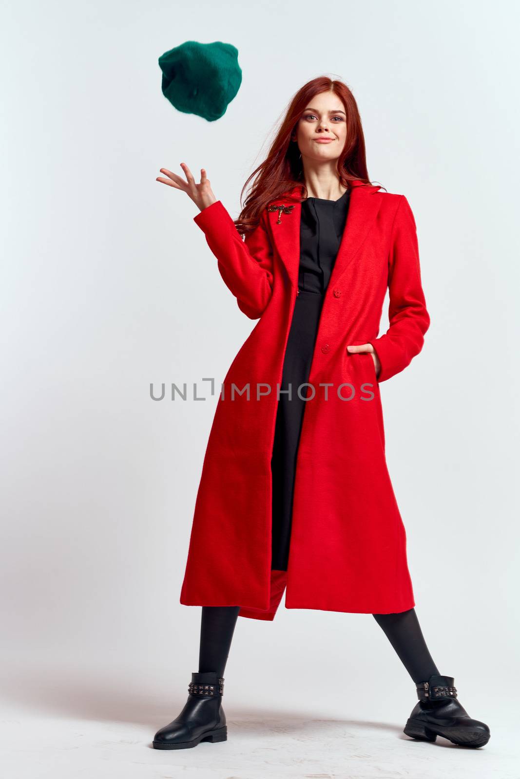 emotional woman in a red coat and with a hat in full growth on a light background black boots pose model. High quality photo