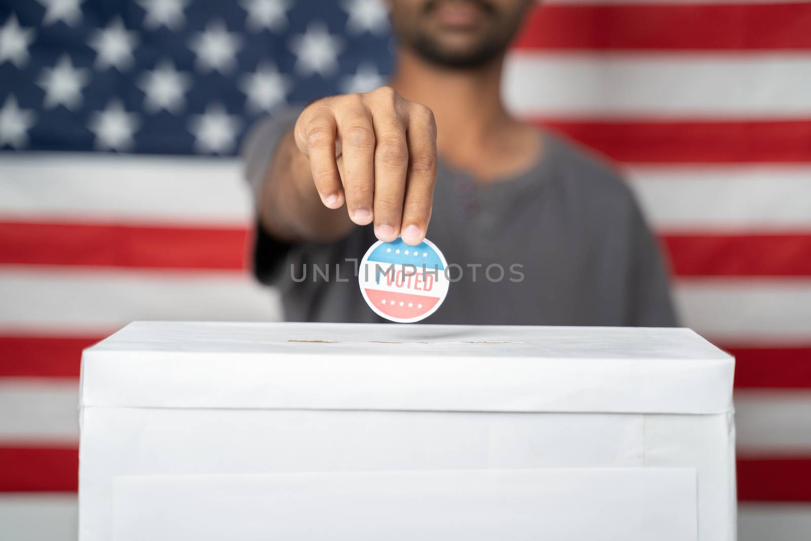 Concept of USA elections, Close up of Hands Putting I Voted sticker inside Ballot box with US flag as background. by lakshmiprasad.maski@gmai.com