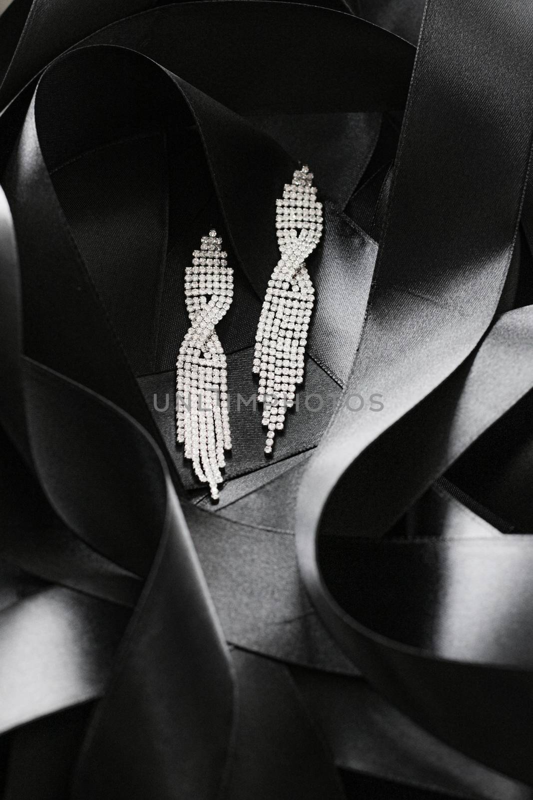 Luxury diamond earrings on black silk ribbon as background, jewelry and fashion brands