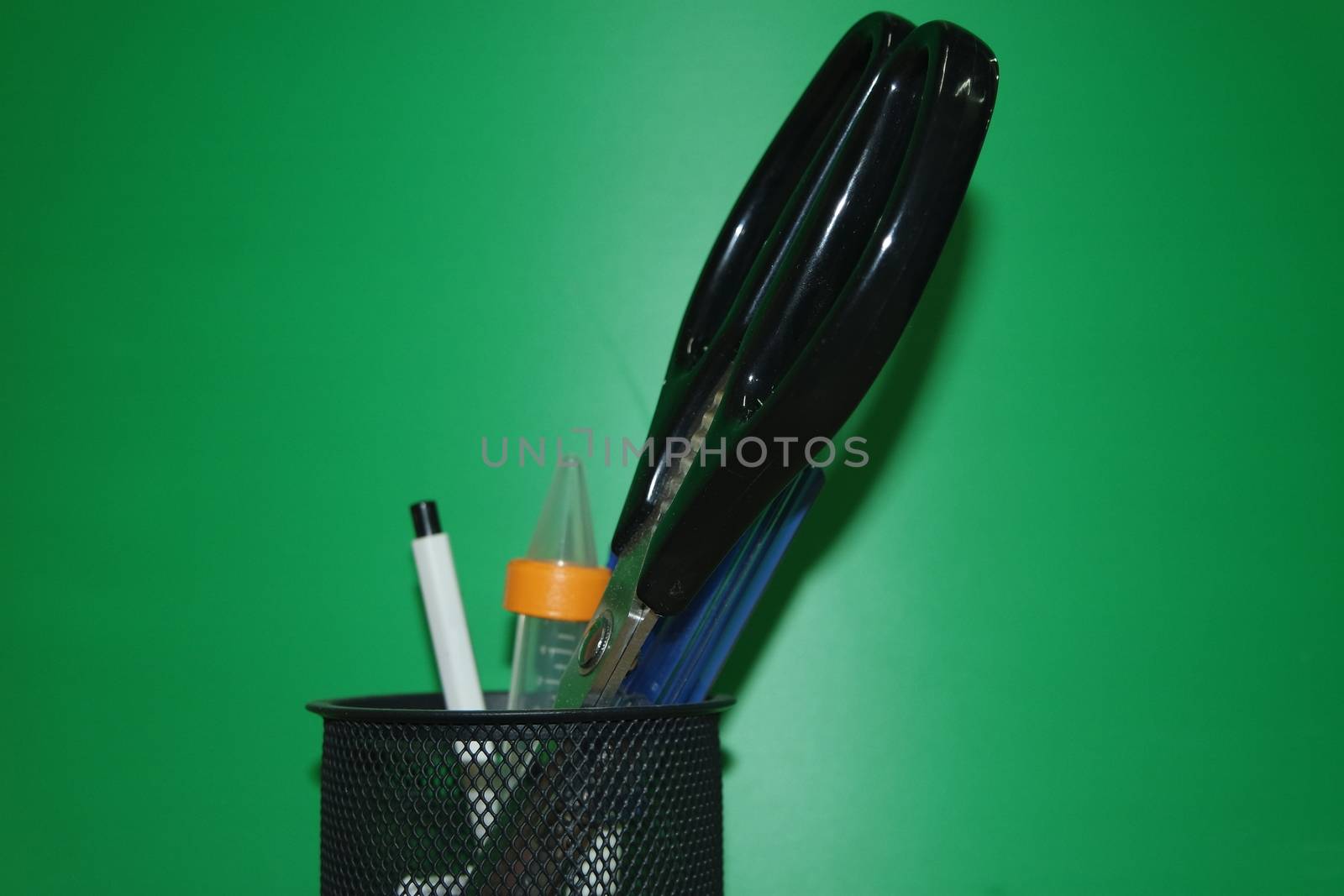 Closeup view of a stationery pot containing stationery items. stationery pot in front of a green background.