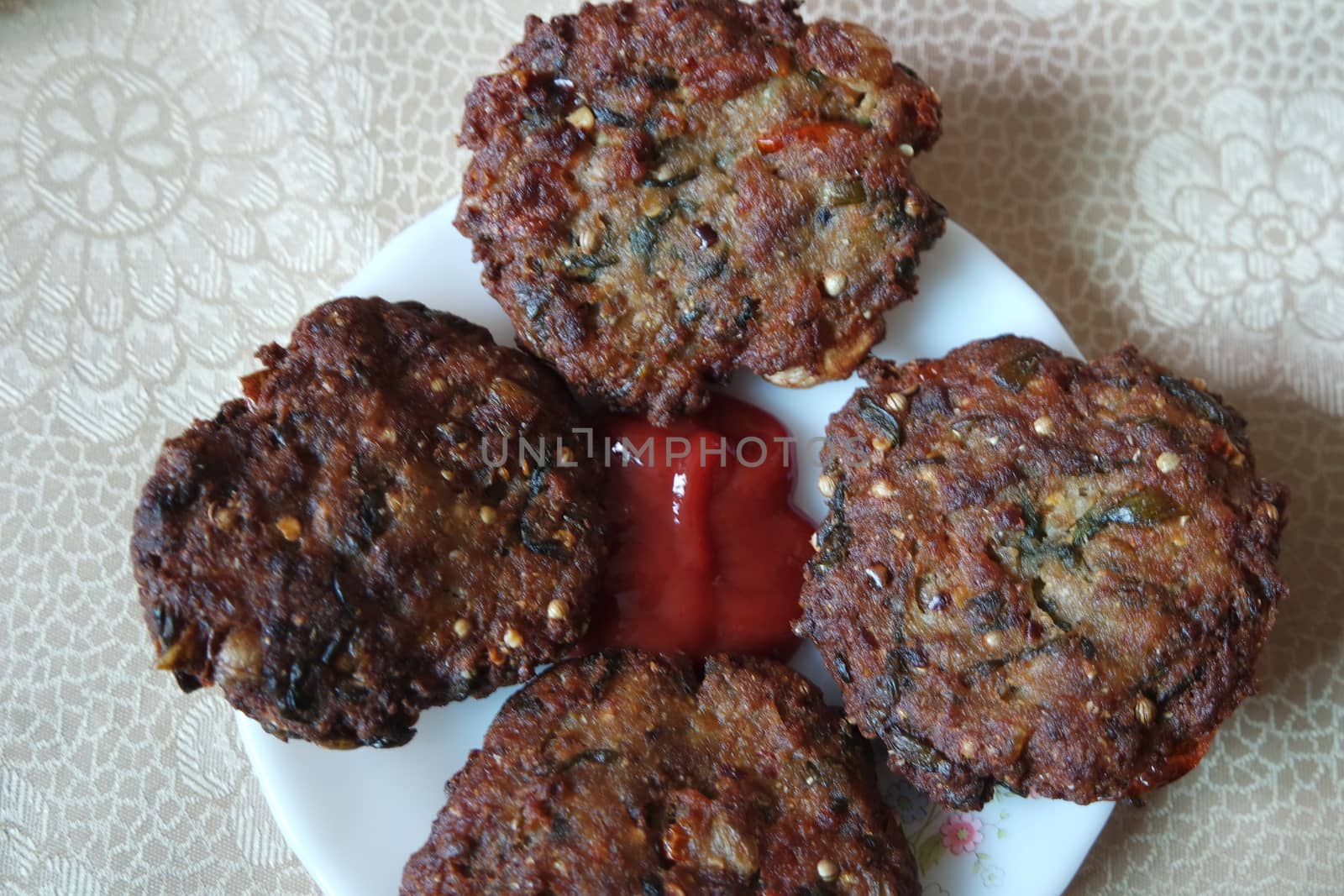 Delicious spicy fried round kebab served in white ceramic plate on a wooden floor with red sauce.