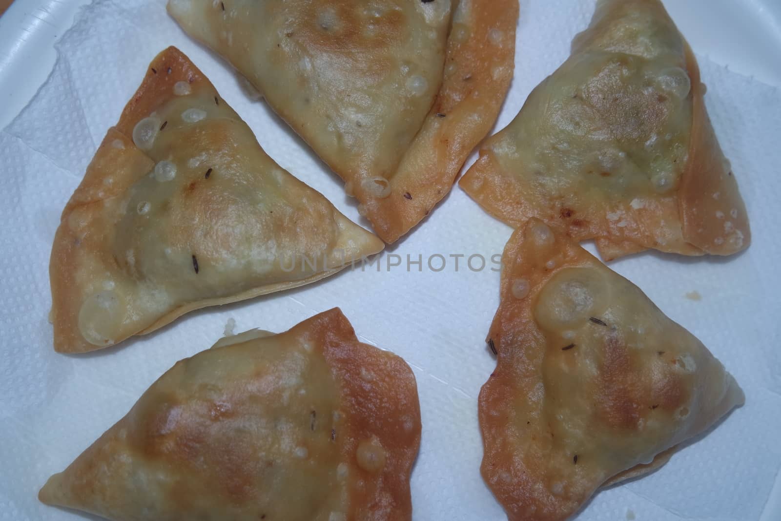 Closeup of delicious home made spicy and crunchy samosa pastries placed in a white ceramic plate on wooden floor