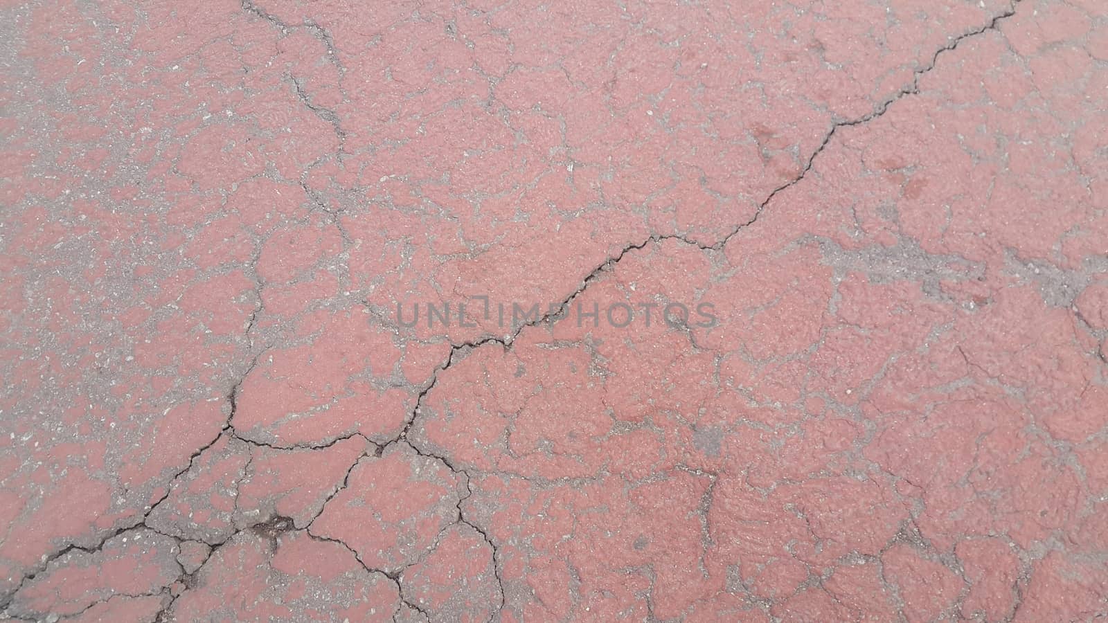Red colored damaged road or paved pathway with crackes of different shpaes. Cracked texture with copy space for text and messages