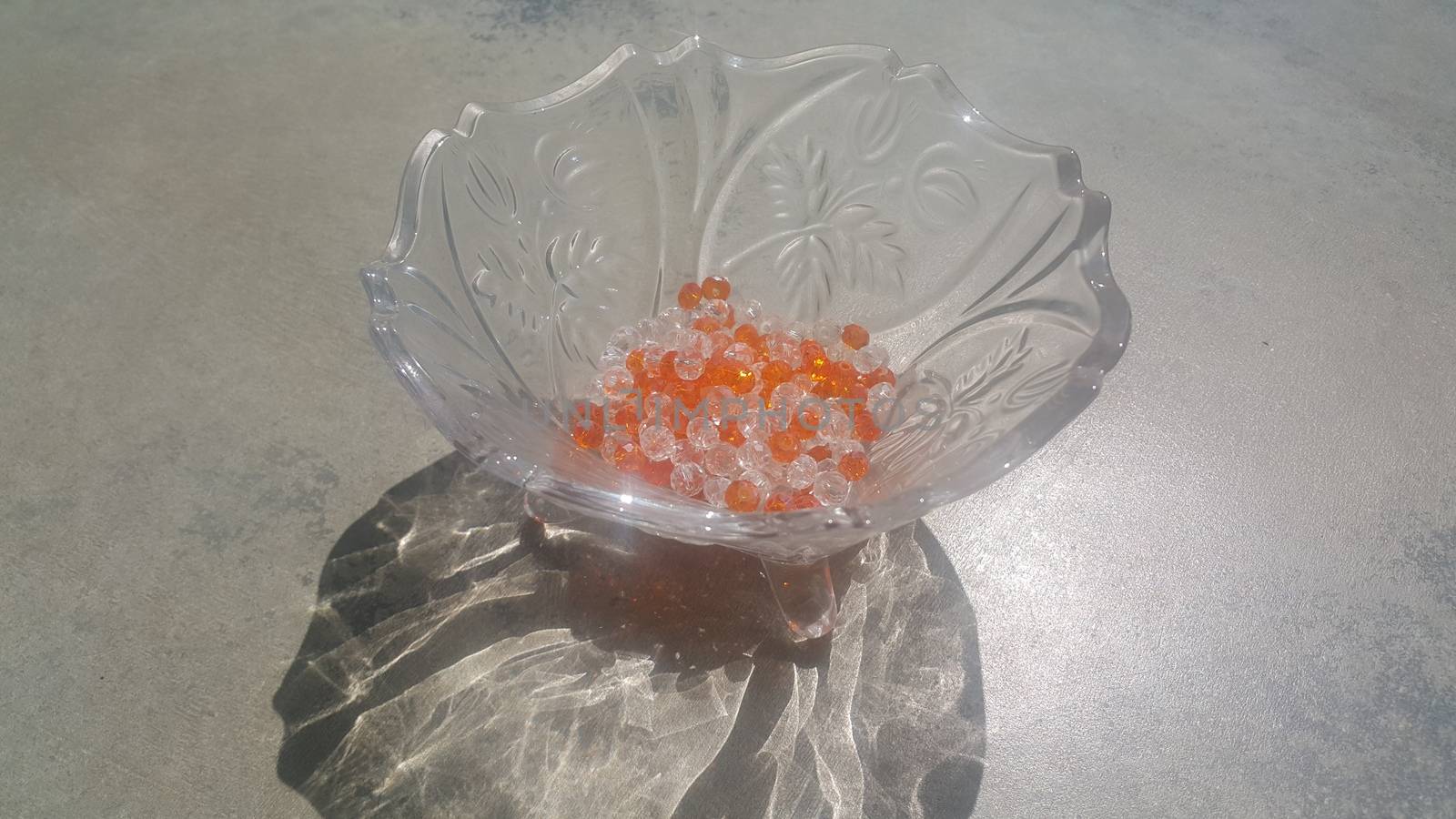 Shining, transparent, orange color crystal beads or gemstones or amber beads in a glass bowl over grey floor