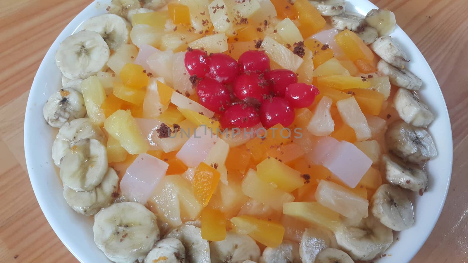 Creamy tasty sweet fruit trifle over custard with banana slices layered on surface on wooden floor. A top view of home made fruit trifle, a products for dessert after meal.