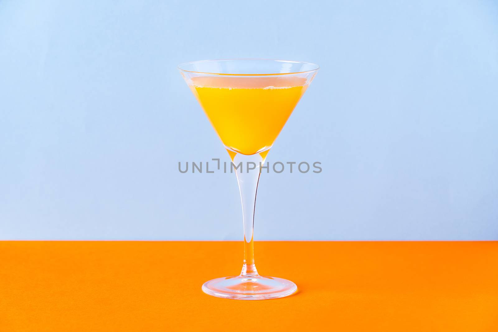 Fresh orange juice in glass on orange surface and light blue background