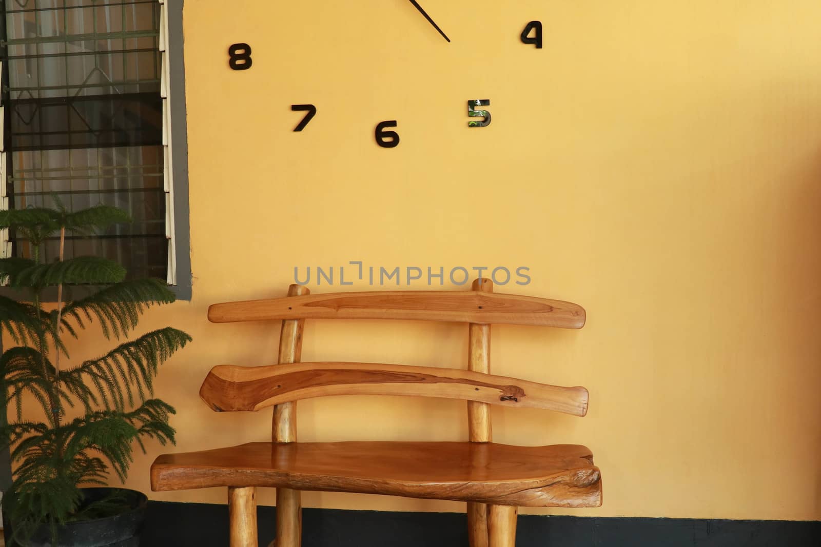 wooden bench near yellow wall. Vintage wooden bench under the wall clock.
