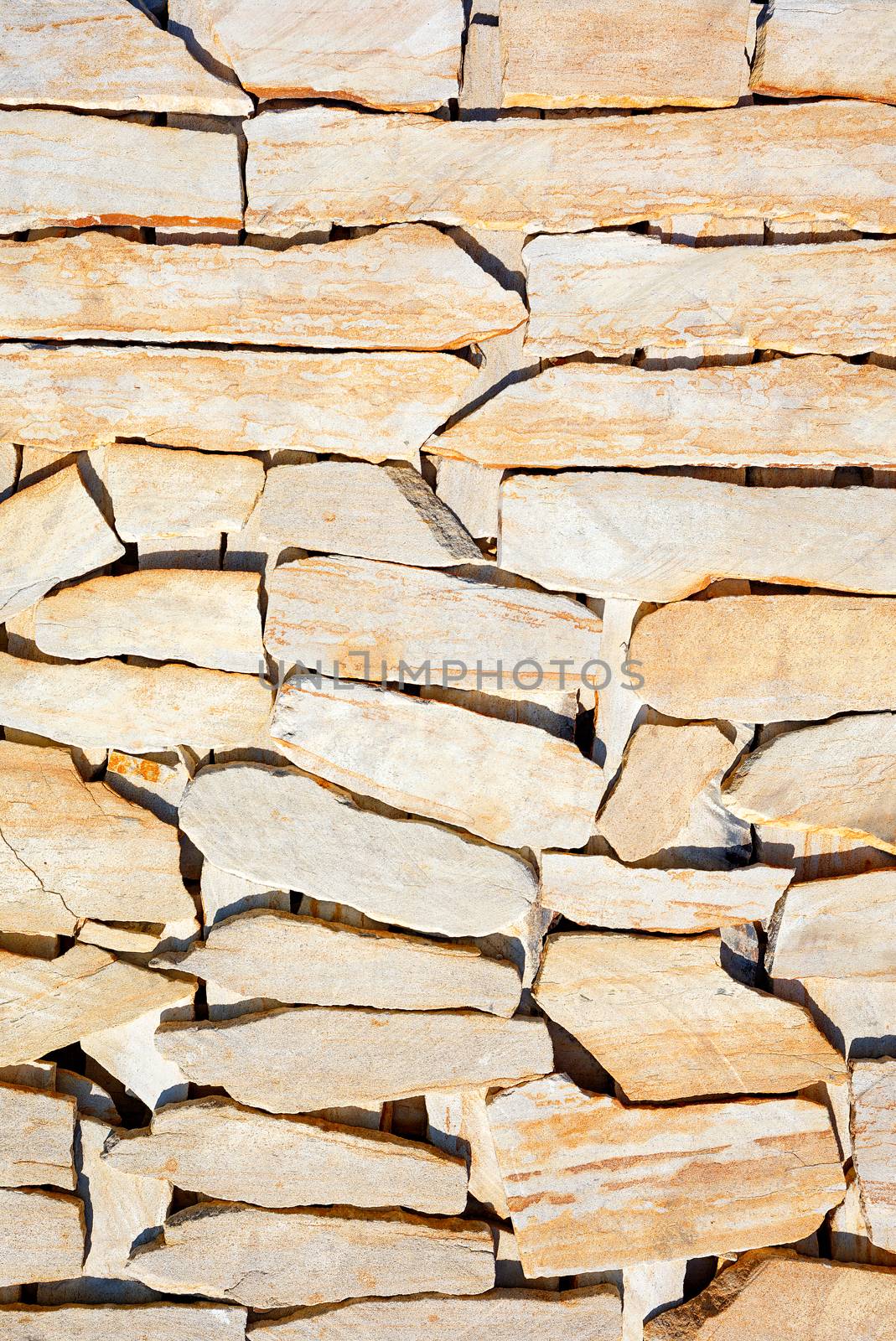 Texture of layered pieces of yellow sandstone stone in harsh sunlight separated by stripes of deep shadow, vertical image.