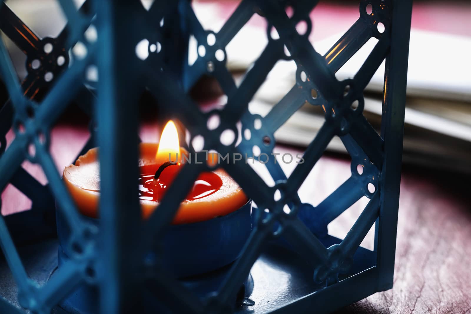 Orange burning candle in blue metal candle holder  , out of focus background