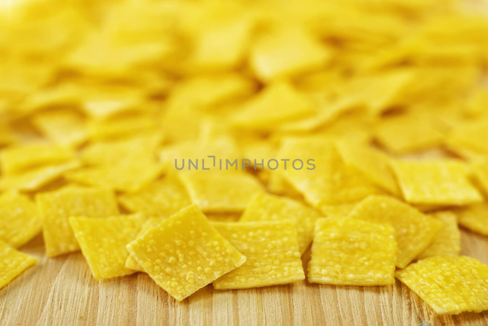 Pile of small flat squares of egg pasta called quadrucci on wooden background,yellow color pasta with rough surface 