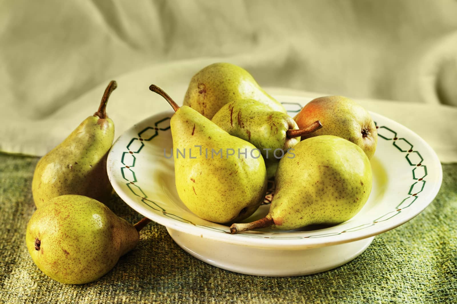 Beautiful green pears on a plate ,green cotton cloth on table and in the background 