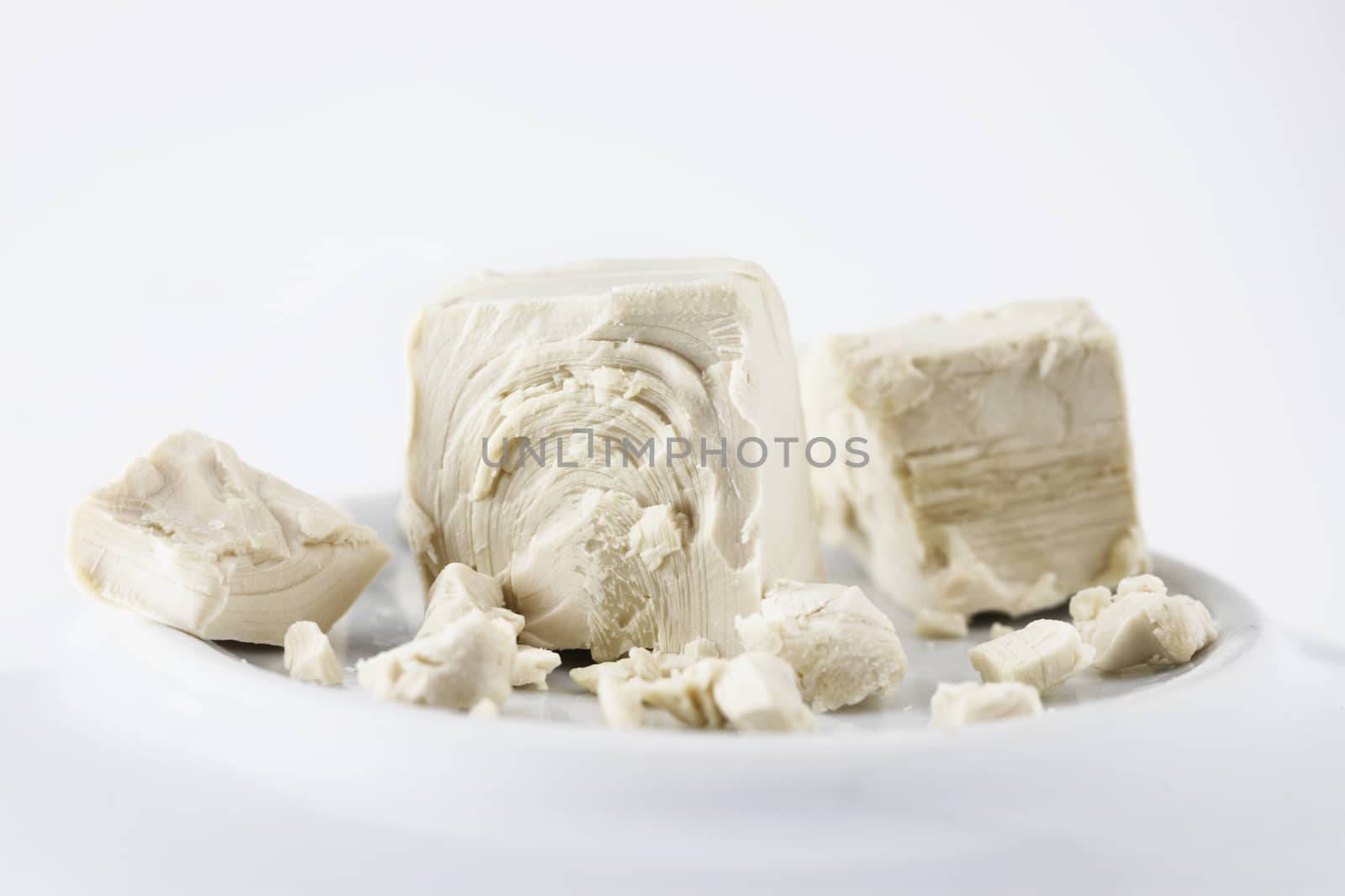 Baking crumbled yeast on white plate ,beige compressed yeast ,soft solid