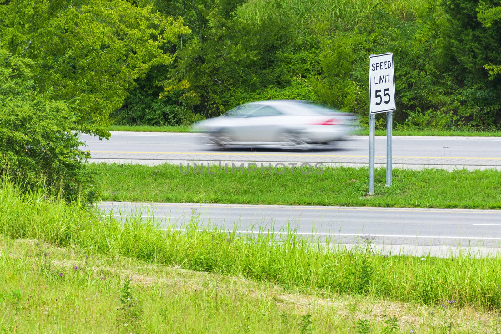 Horizontal shot of a speeding car streaking by a speed limit sign.  Blurring shows motion.
