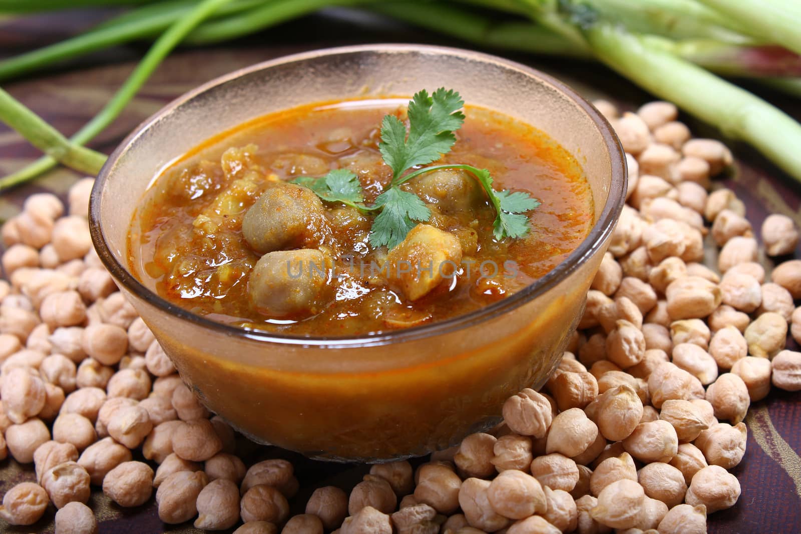 spicy chana masala, raw chickpeas around the bowl with green onion
indian dish