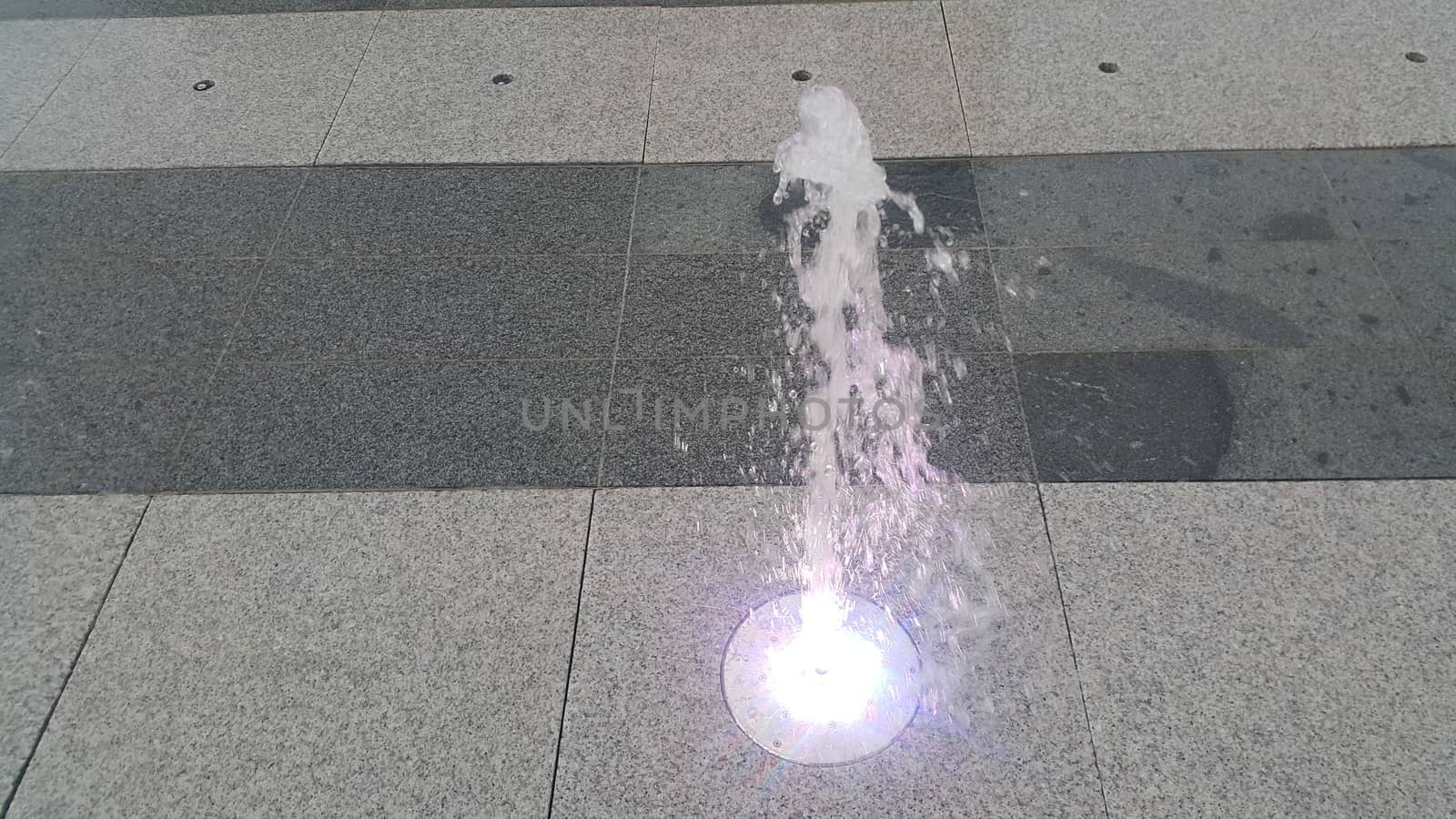 Beautiful and colorful light water fountain over concrete floor by Photochowk