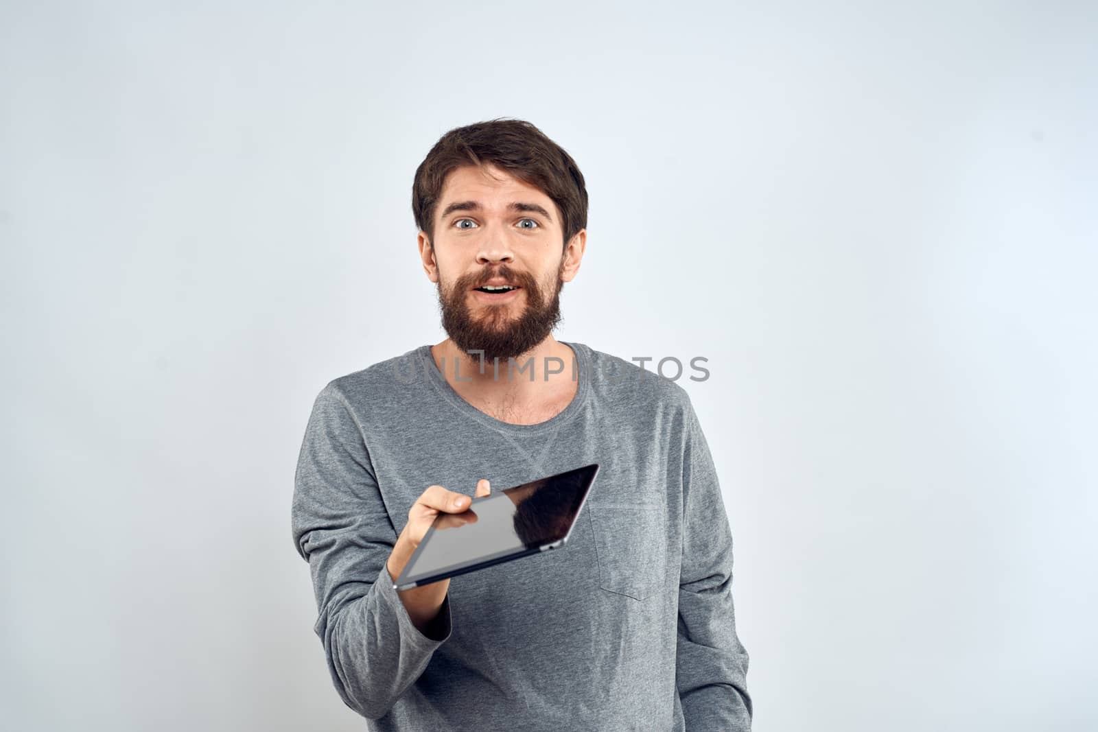 A bearded man with a tablet in his hands a gray jacket technology internet light background. High quality photo