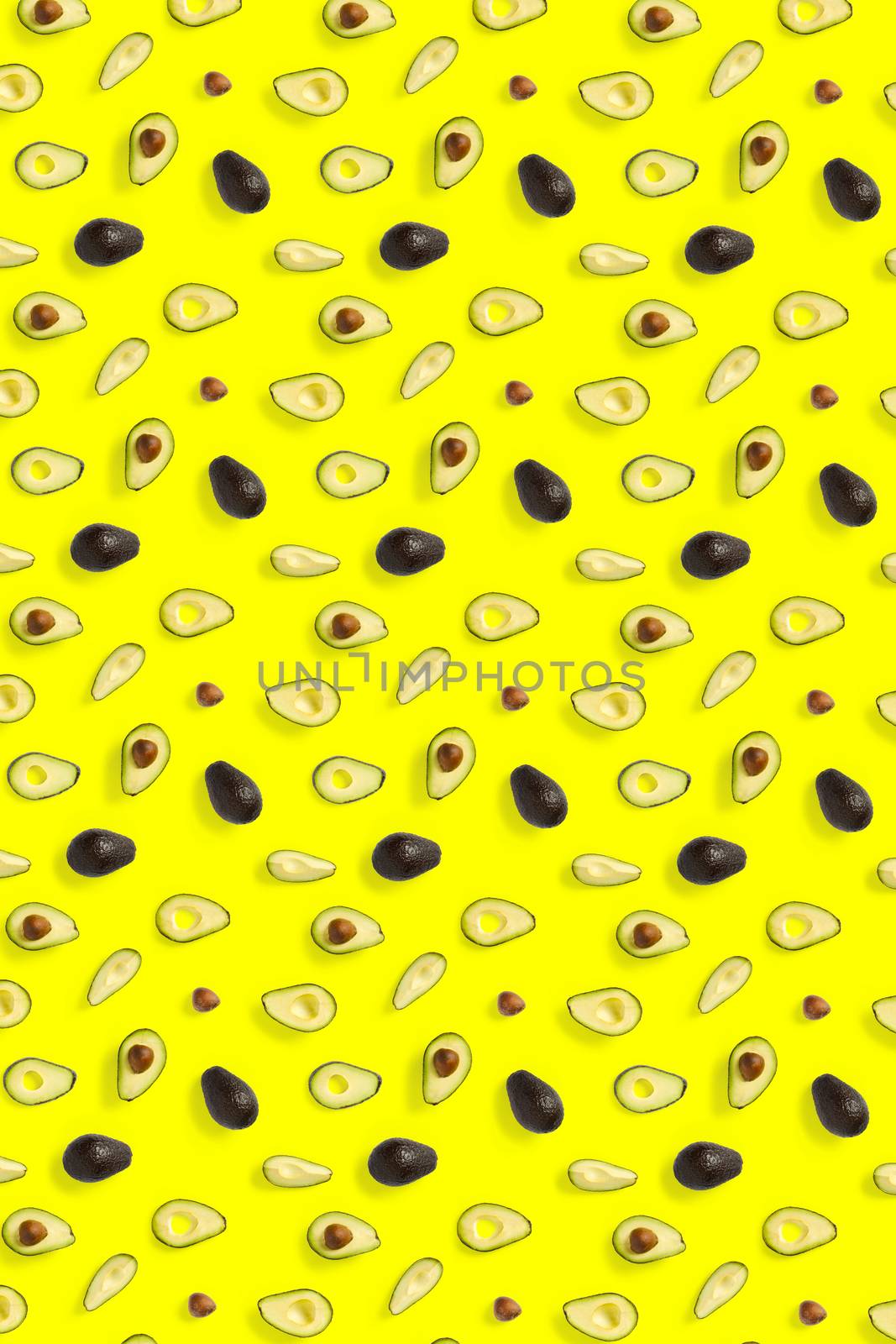 Avocado. Background made from isolated Avocado pieces on yellow background. Flat lay of fresh ripe avocados and avacado pieces. by PhotoTime