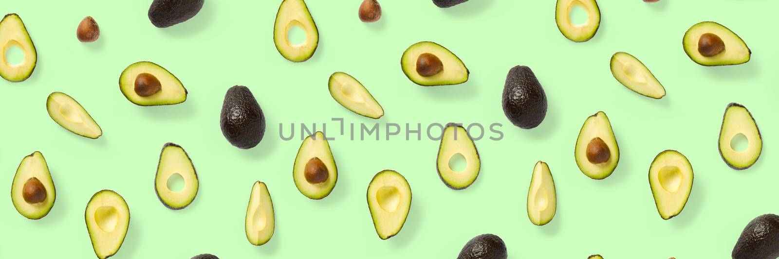 Avocado banner. Background made from isolated Avocado pieces on green background. Flat lay of fresh ripe avocados and avacado pieces. by PhotoTime
