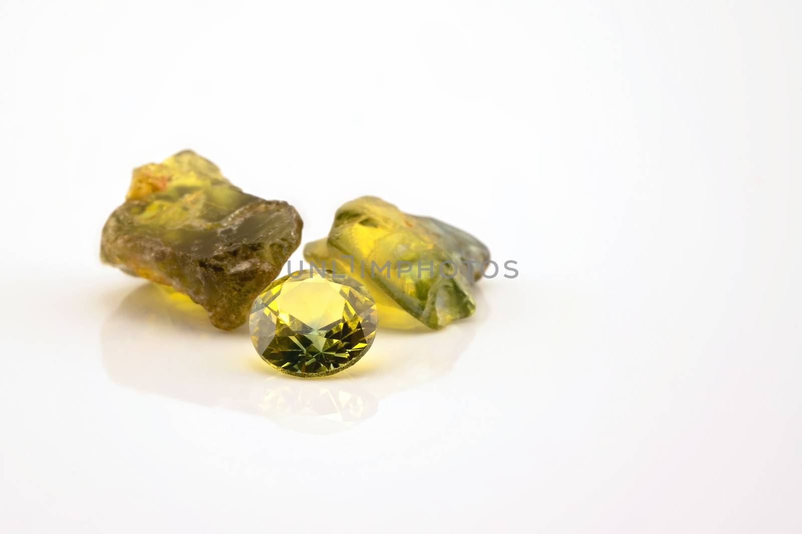One round facet cut yellow green sapphire with two uncut natural sapphires of a similar colour, isolated on a white background