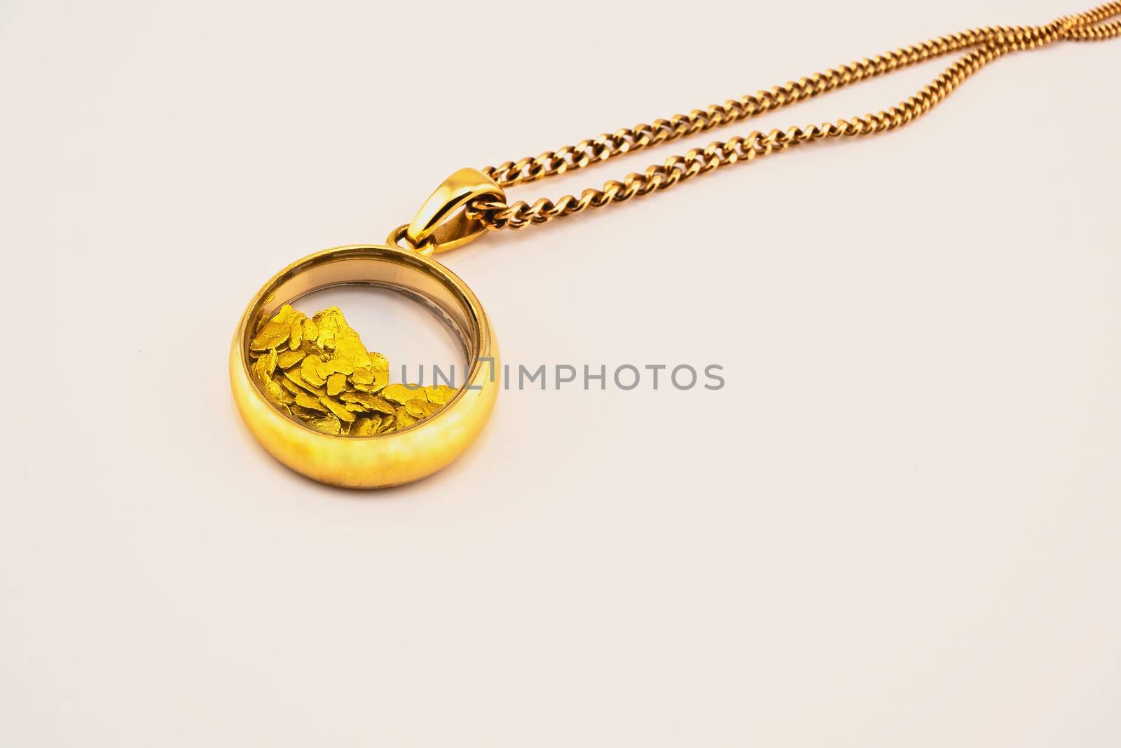 A round gold pendant with glass enclosing gold nuggets, attached to a rose gold chain
